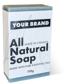 A bar of blue-green all-natural soap with a white label. The label features a placeholder for 'YOUR BRAND' and text indicating the 110g soap is 'Made in Canada' with pure essential oils.
